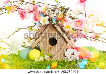 Easter decoration with birdhouse and eggs on green grass. Spring apple and cherry blossoms. Retro style toned picture with light leaks.