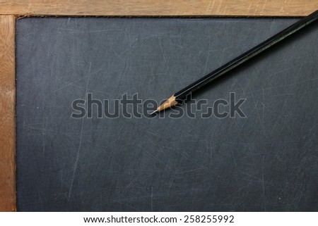 Vintage and old slate blackboard and wooden pencil put on the black color leather background represent the teaching equipment related.