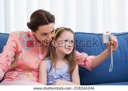 Mother and daughter taking selfie at home in the living room