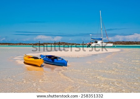 blue and yellow kayaks beached along the white sand with catamaran sailboat anchored in the background.