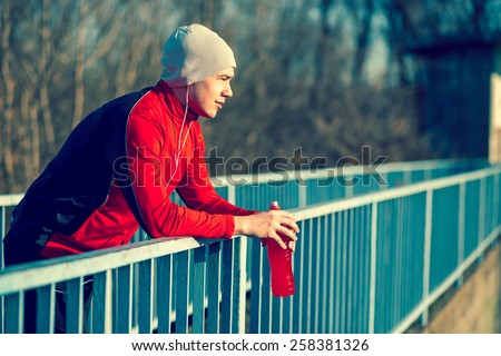 Athlete relaxing after an intense workout, holding a bottle of an energy drink Royalty-Free Stock Photo #258381326