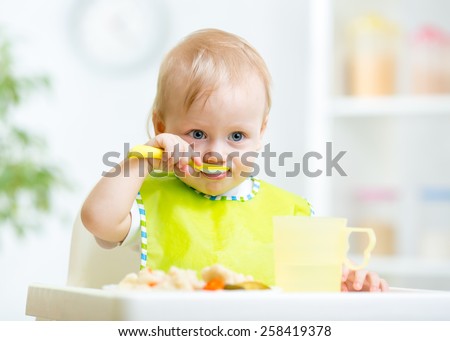 happy baby child sitting in chair with a spoon Royalty-Free Stock Photo #258419378