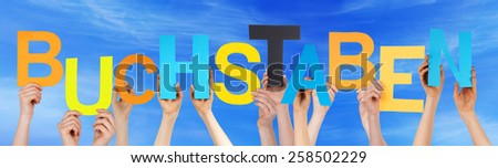 Many Caucasian People And Hands Holding Colorful Letters Or Characters Building The German Word Buchstaben Which Means Letters On Blue Sky