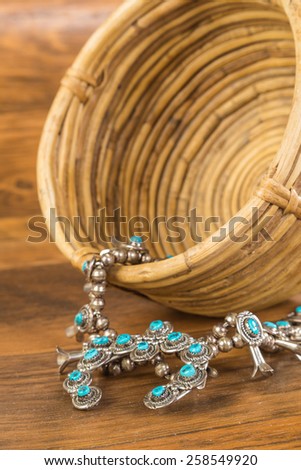 Traditional Native American Turquoise and Silver Squash Blossom and vintage spiral woven wicker basket on rustic wooden background.