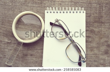 vintage reading glasses, magnifying loupe, note pad, diary, diary on wooden background