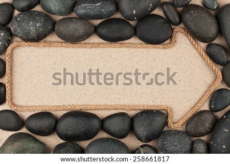Pointer made of rope with  black stones, lying on the sand
