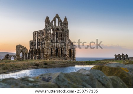 Stone ruins of Whitby Abbey on the cliffs of Whitby, North Yorkshire, England at sunset. Royalty-Free Stock Photo #258797135