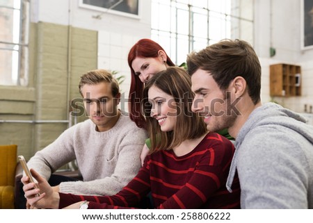 Smiling Young White Friends Watching Something at Mobile Phone While Resting at the Living Room. Royalty-Free Stock Photo #258806222