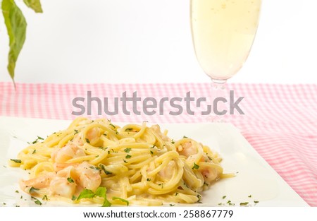 Fettuccine Alfredo with shrimp and glass of white wine on pink gingham in bright back light.