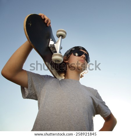 Young boy with skateboard in hand against the sky
