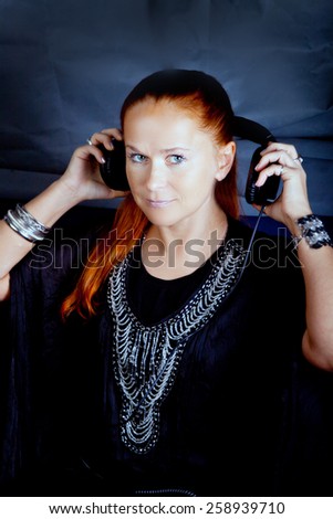 Attractive woman in classic outfit takes off the headphones (tinted portrait on gray-blue background)