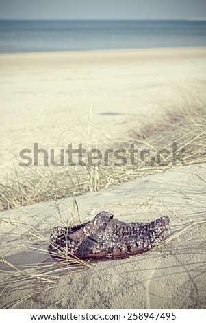 Retro filtered photo of an old weathered shoe washed up on beach.