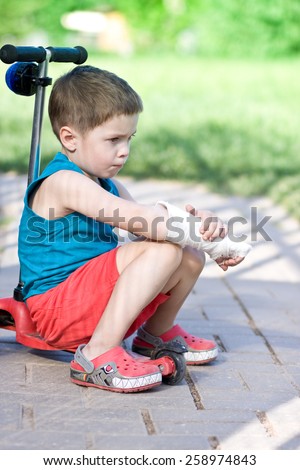 	Sad boy with broken arm sits on scooter
