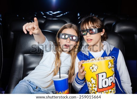 Girl showing something to sister while having snacks at 3D cinema theater