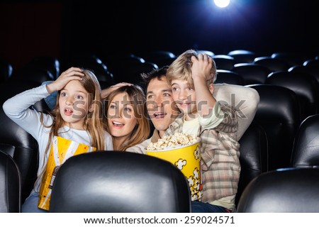 Amazed family with hands on heads watching movie in cinema theater