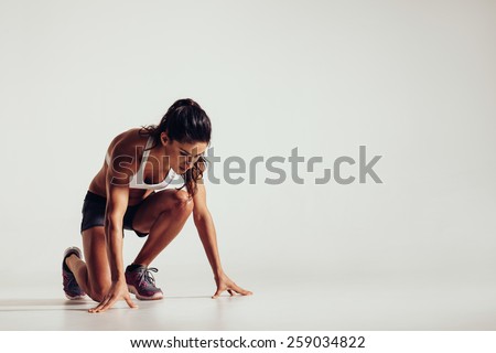 Healthy young woman preparing for a run. Fit female athlete ready for a spring over grey background with copy space. Royalty-Free Stock Photo #259034822