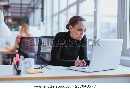 Image of woman using laptop while sitting at her desk. Young african american businesswoman sitting in the office and working on laptop. Royalty-Free Stock Photo #259040579