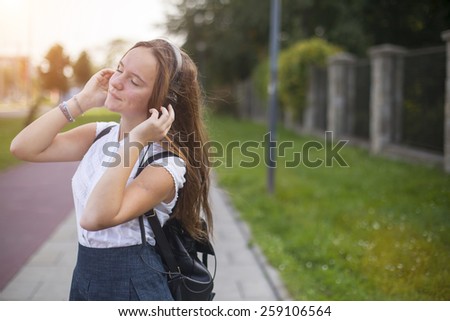 Young cute girl enjoying music with headphones outdoors in the mild sunshine.