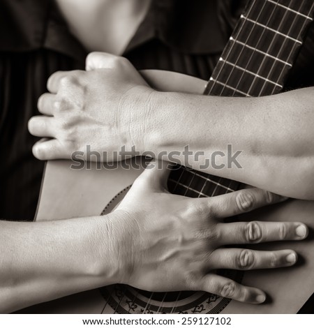 Classic guitar closeup in sepia - Musician hands embracing a classic acoustic guitar