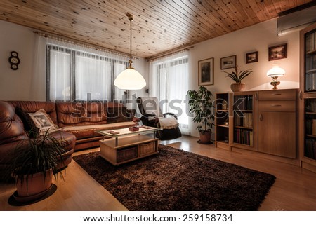 Classically furnished living room in wooden design with old fashioned accessories like lights, wooden clock, pictures on the wall and so on. The room is warm and cozy.