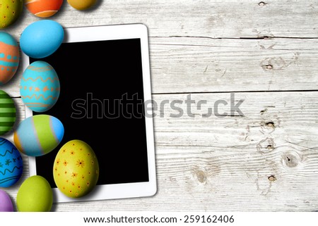 painted eggs and tablet with blank screen on a wooden table