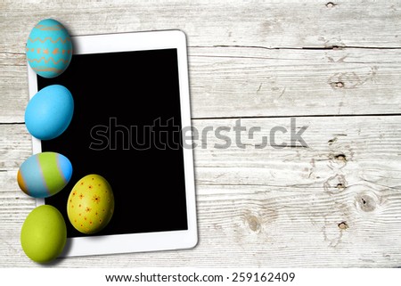 painted eggs and tablet with blank screen on a wooden table