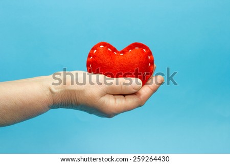 Red heart in old senior woman hand on blue background
