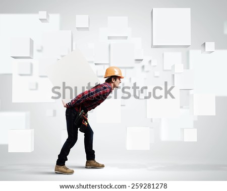 Young builder man in hardhat carrying white blank cube on back