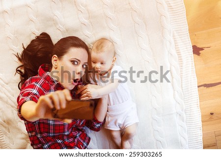 Cute little baby girl and her mother taking selfie on a blanket in a living room.