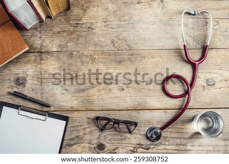 Workplace of a doctor. Stethoscope, clip board, books, glasses and other things on wooden desk background.