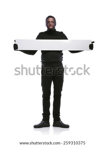 Thief with balaclava on his face, dressed in black, holding an empty banner. Studio shot on white background.