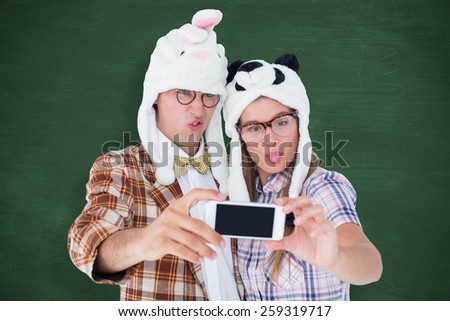 Geeky hipster couple taking selfie with smart phone against green chalkboard