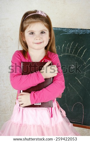 Little girl holding book and standing in front of the blackboard