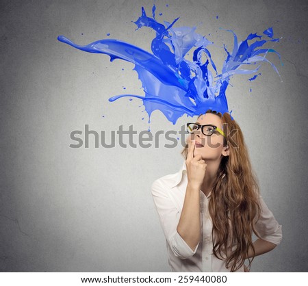 Thoughtful businesswoman looking up with colorful splashes coming out of her head isolated on gray wall background. Face expression perception 