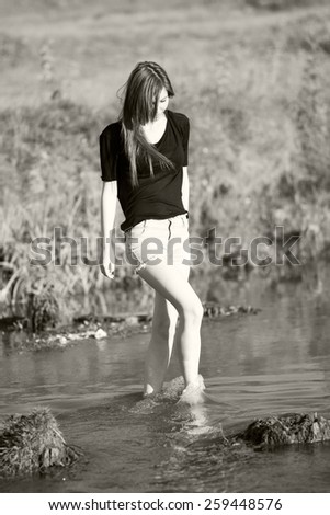 Beautiful girl with long, straight hair posing and playing with water in a small river. Black and white, artistic photography