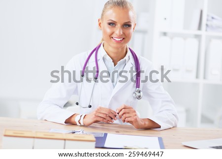 Beautiful young smiling female doctor sitting at the desk 