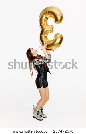 Beautiful brunette girl having fun and holding yellow balloon in hands. Slim body, natural makeup, pink lips. Laughing. Inside. White background, not isolated