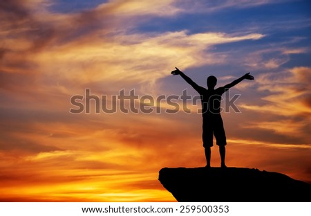 Silhouette of a man on a mountain top on fiery orange background 