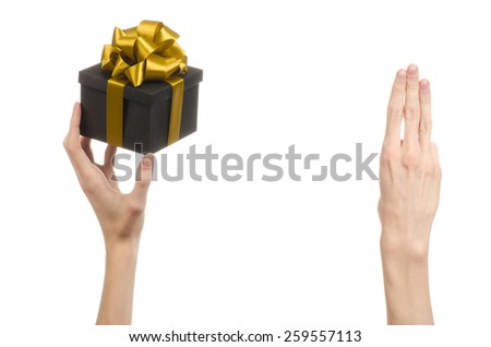 The theme of celebrations and gifts: hand holding a gift wrapped in a black box with gold ribbon and bow, the most beautiful gift isolated on white background in studio