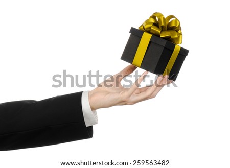 The theme of celebrations and gifts: a man in a black suit holding a exclusive gift packaged in a black box with gold ribbon and bow, the most beautiful gift isolated on white background in studio