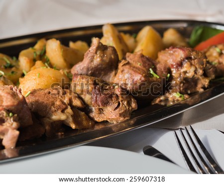 Baked meat with potato on metal plate, shallow field of depth, focus on middle pieces of meat
