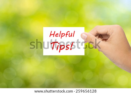 Hand holding a paper Helpful Tips ! on green background 