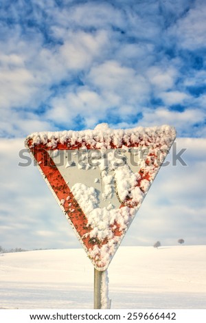 give way road sign, traffic sign, yield sign, with blue sky and clouds and with snow in winter season