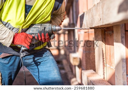 Worker using a drilling power tool on construction site and creating holes in bricks  Royalty-Free Stock Photo #259681880