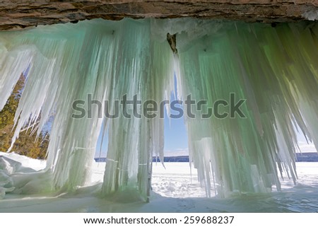 Ice curtains drape from a cavern entrance on Lake Superior's Grand Island in Munising Michigan. Pictured Rocks National Lakeshore can be seen in the background of this winter scene.