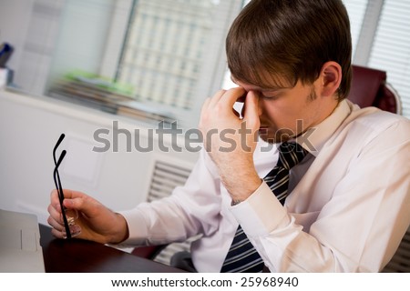 Photo of fatigue man with his eyeglasses off keeping his hand near face after hard working day