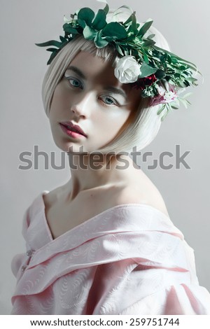 Portrait of a beautiful young blond woman with short hair and a wreath of flowers in the studio