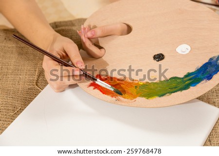 Macro photo of young female artist dipping paintbrush in paint on pallet