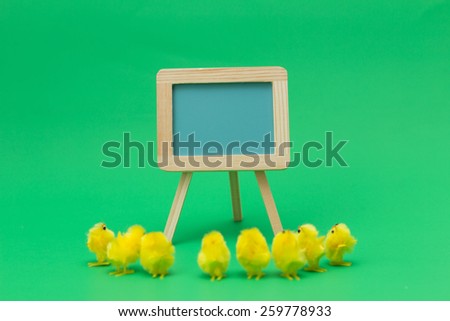 Easter chicks gathered around blue pastel chalkboard on green background