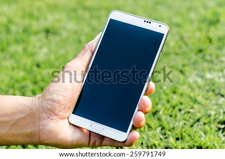 Man hand holding smartphone against spring green grass background soft focus.